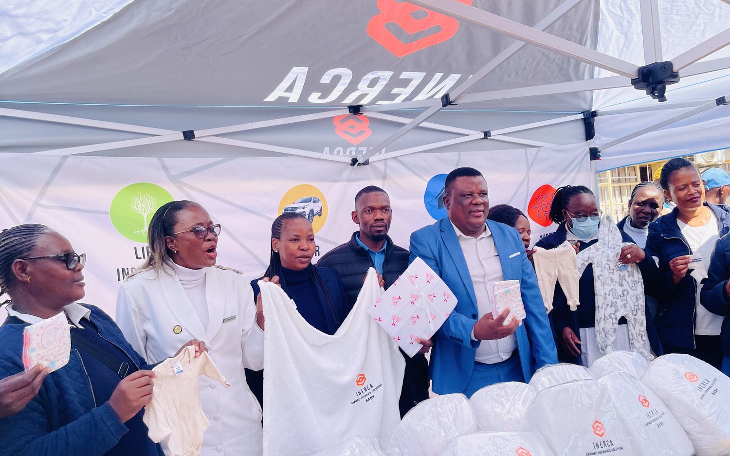 Nurses, dignitaries and INERCA staff holding up donated baby clothes beside a table of bundles